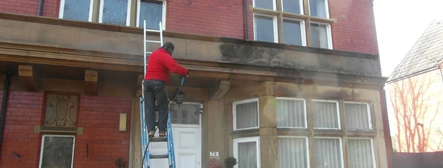 Cleanwalls operative removing years of grime from a red brick and stone frontage