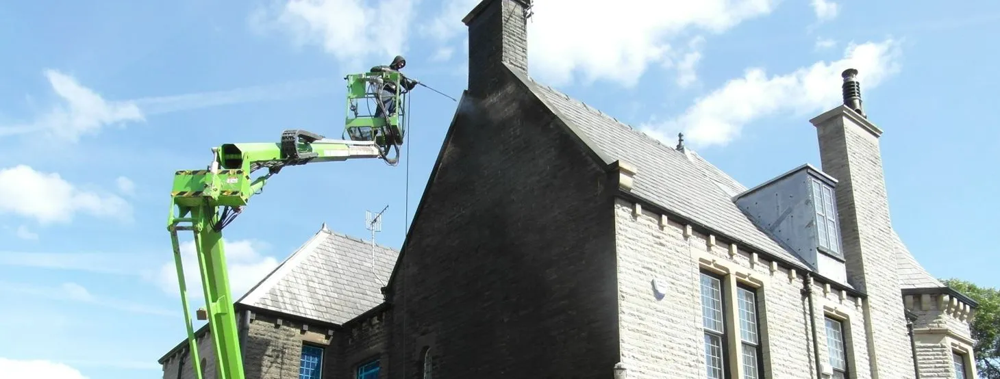 Cleanwalls operative jet washing soot from a large stone house from a cherry picker